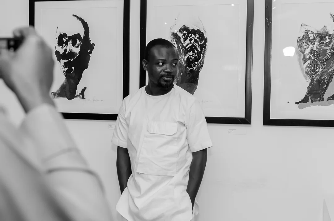 An artist standing in front of a series of expressive portraits.