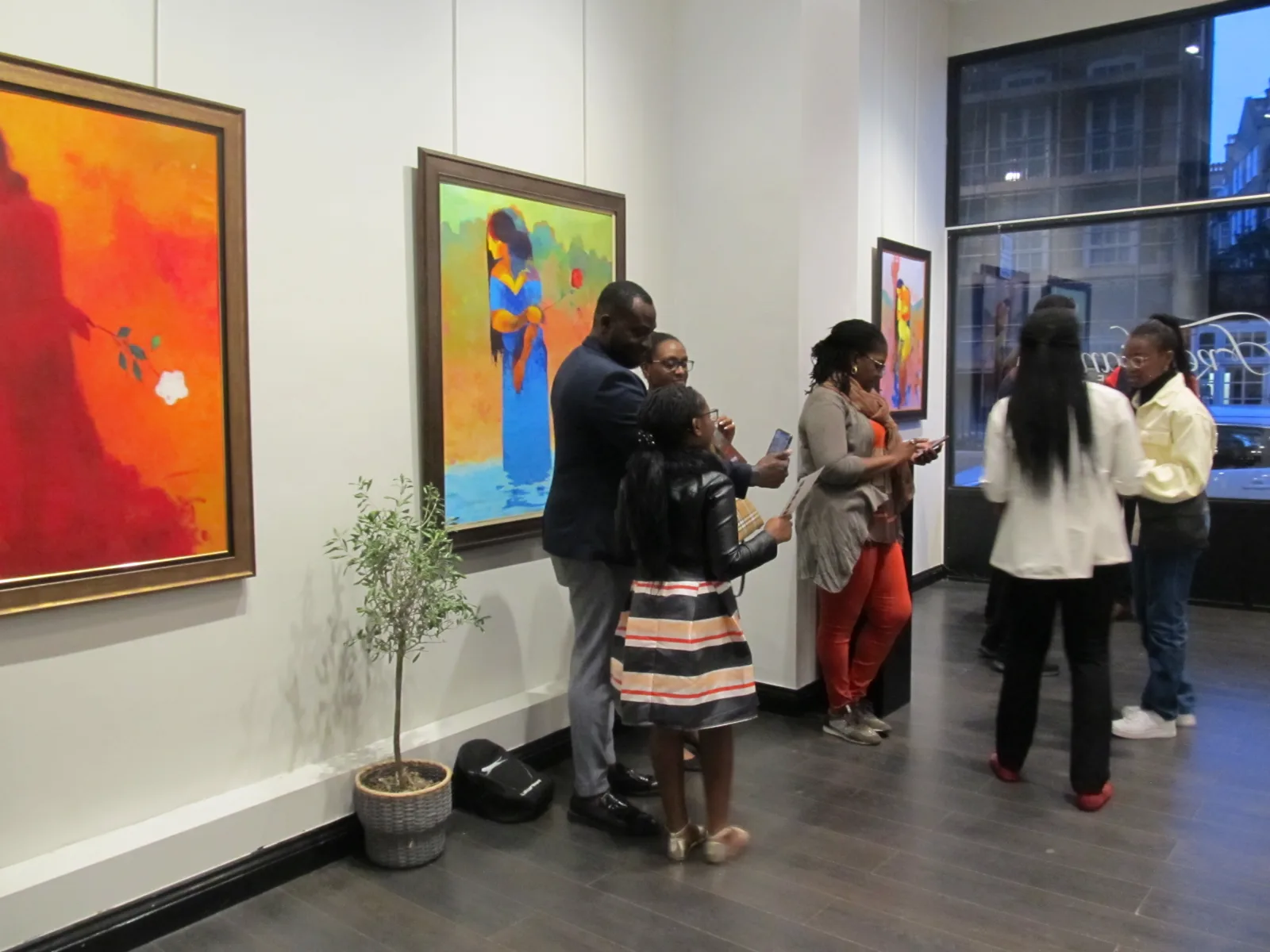 Visitors gathering among colourful paintings at an exhibition opening.