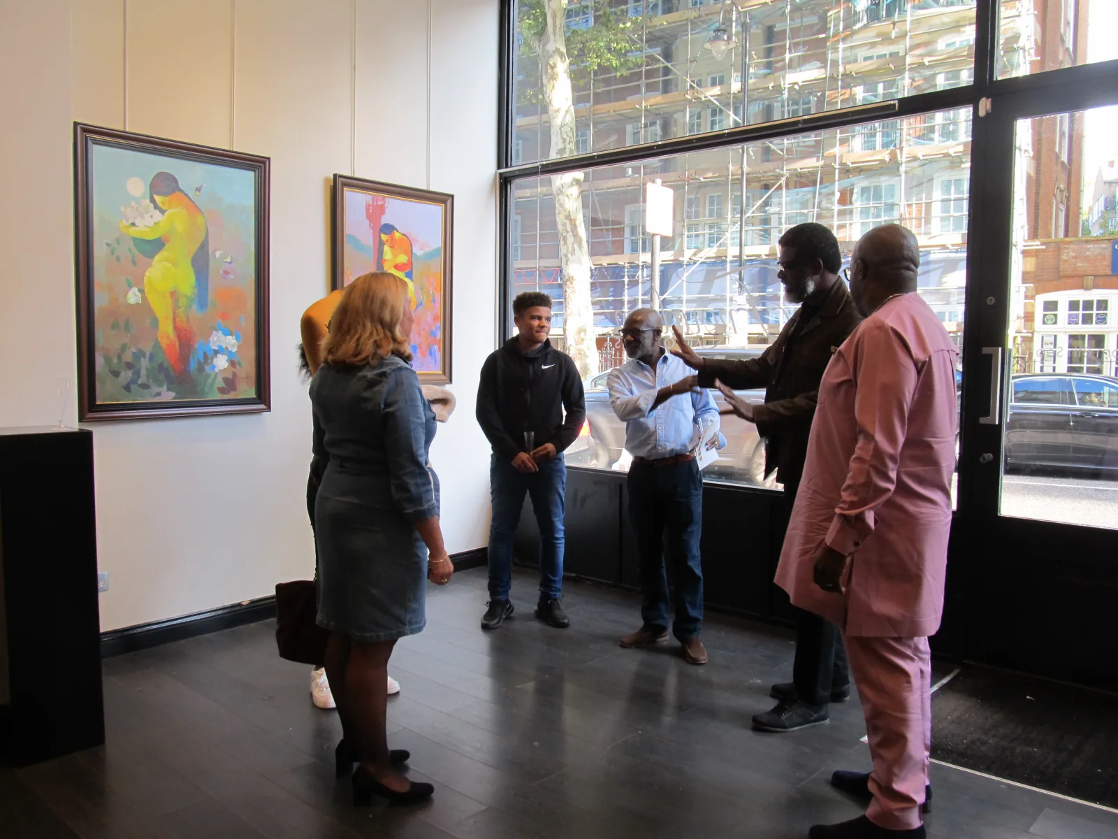 Visitors in conversation beside paintings and the gallery window.
